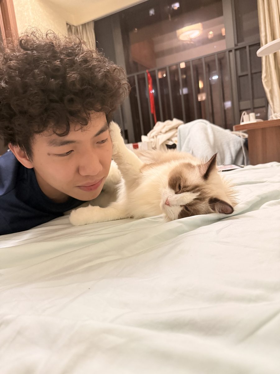 Jimmy lying on a bed beside his ragdoll cat